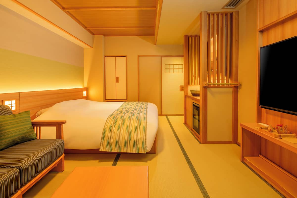 A hotel room with a bed, a sofa, a television, a wooden cabinet, and a sliding door.