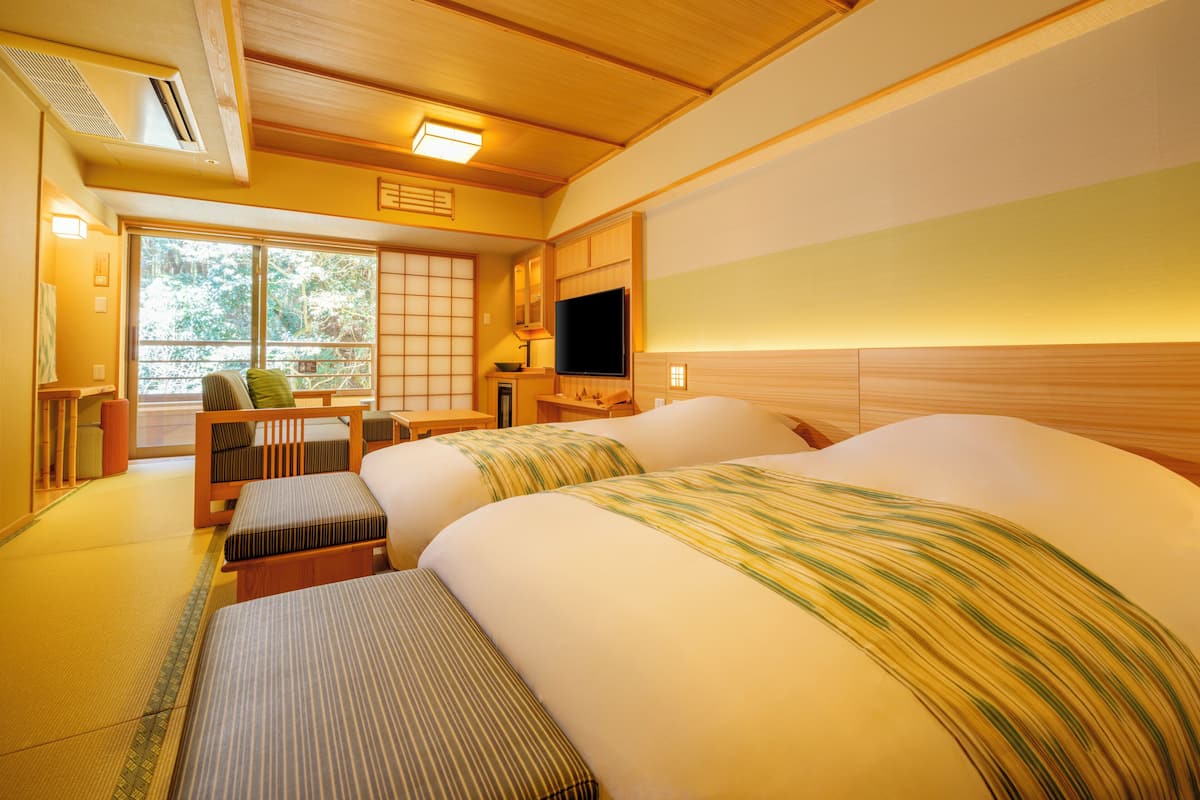 A hotel room with a traditional Japanese aesthetic, featuring tatami flooring, a low wooden ceiling, and a sliding shoji screen.