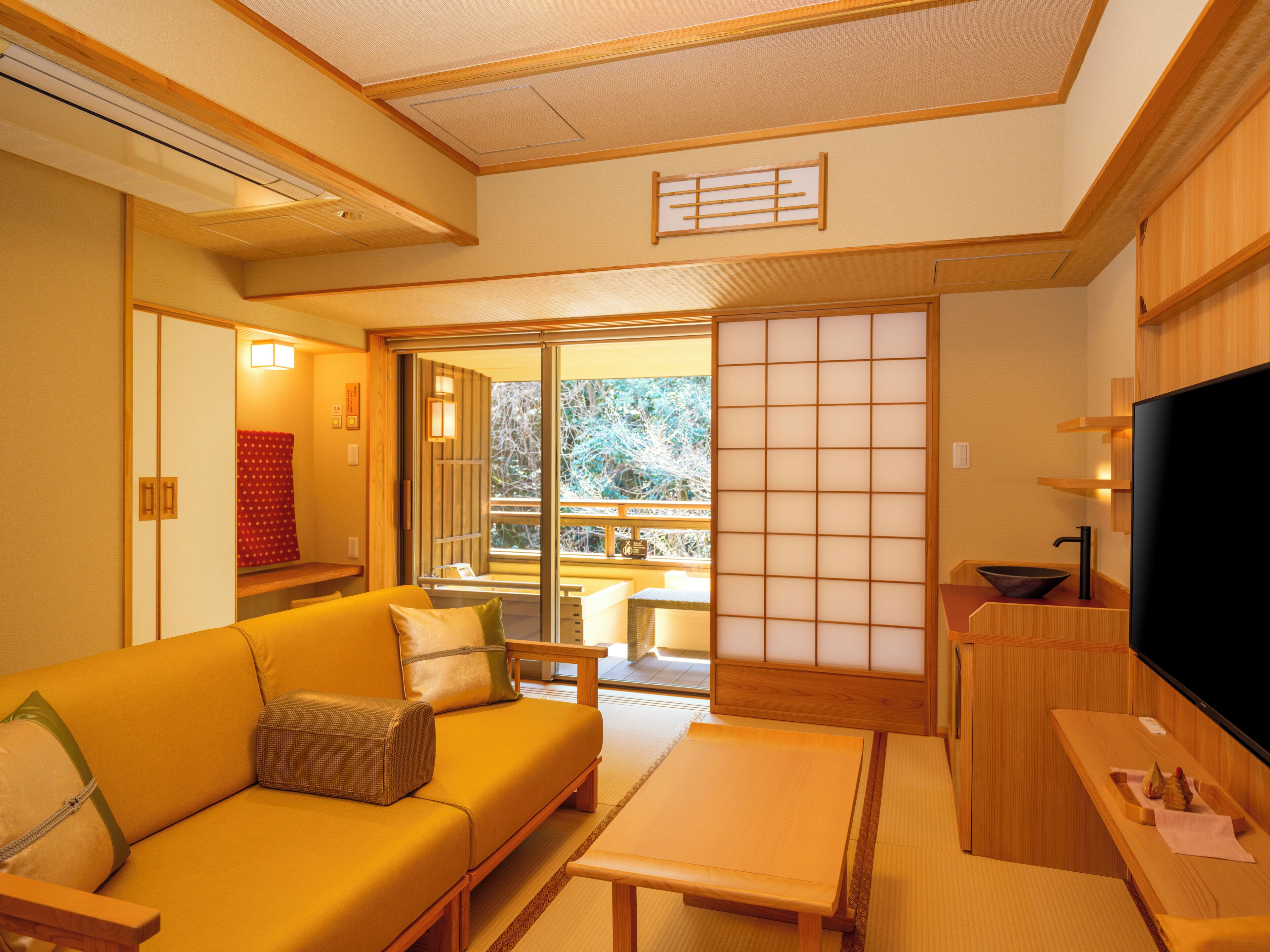 Et traditionelt japansk værelse med tatamimåtter, et lavt træbord, en sofa og en skydedør af glas, der fører ud til en balkon.