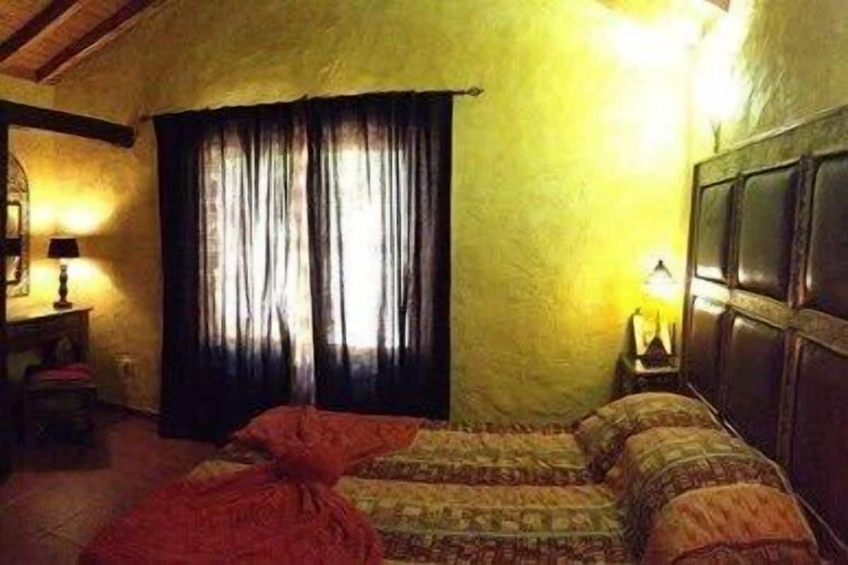 A room with a bed, a nightstand, a lamp, and a window with curtains.