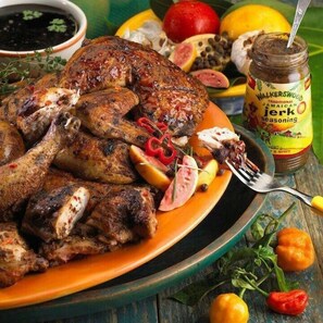 Un poulet rôti, accompagné de divers légumes et d’un bocal d’épices à la jamaïcaine, présenté sur une assiette.