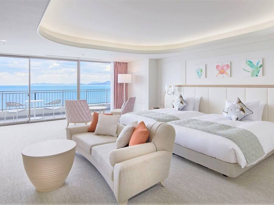 Une chambre d’hôtel moderne dotée d’un grand lit, d’un canapé, d’une table ronde et d’un balcon offrant une vue sur la mer.