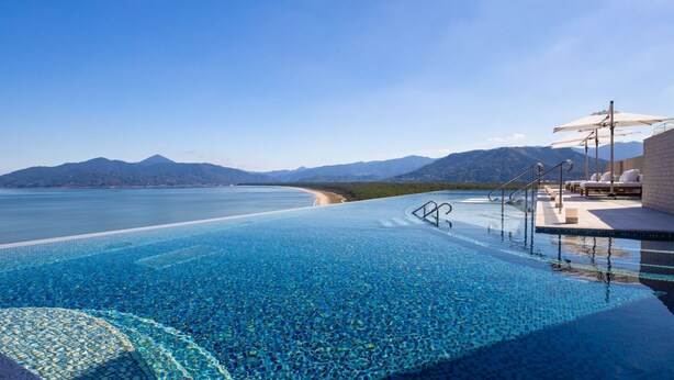 A infinity pool with clear blue water, a beach, and mountains in the background. - Karatsu Seaside Hotel (Karatsu)