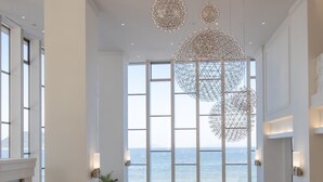 A spacious room with large windows overlooking the sea, modern seating, and a unique chandelier. - Karatsu Seaside Hotel (Karatsu)
