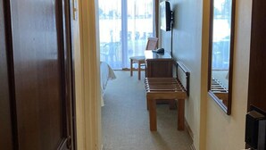 Un pasillo de hotel con un banco de madera, una silla y una cama al fondo.