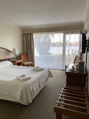 A hotel room with a bed, a desk, a chair, a TV, and a view of a pool through large windows.