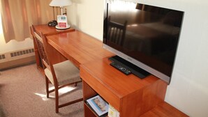 Una habitación de hotel con un escritorio de madera, un televisor, una lámpara y una silla.
