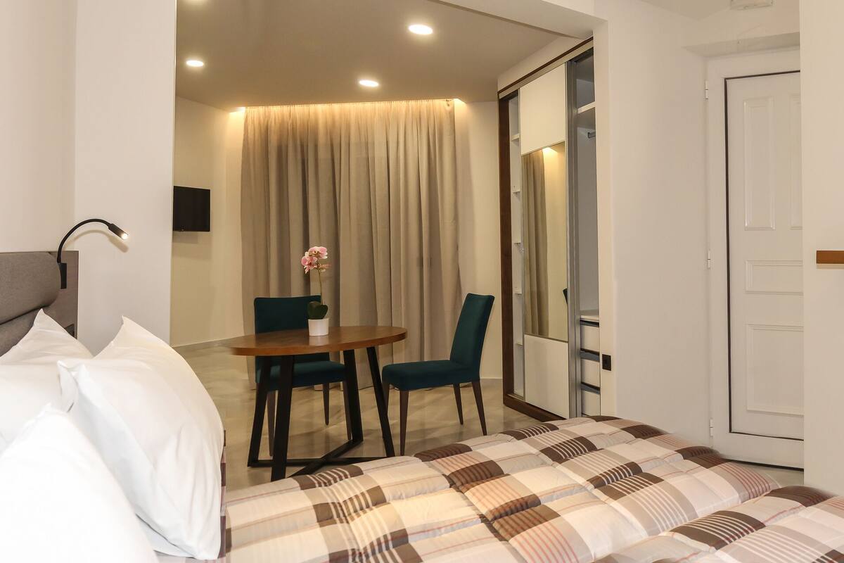 Ein Hotelzimmer mit einem Bett, einem kleinen Tisch mit Stühlen, einem Schreibtisch, einem Spiegel und einem durch eine offene Tür einsehbarer Badezimmer.