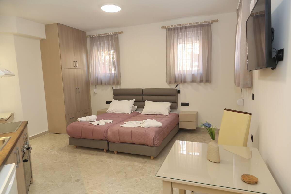 Ein Schlafzimmer mit einem Bett, Nachttischen, einem Fernseher und einem Schreibtisch mit einer Vase.