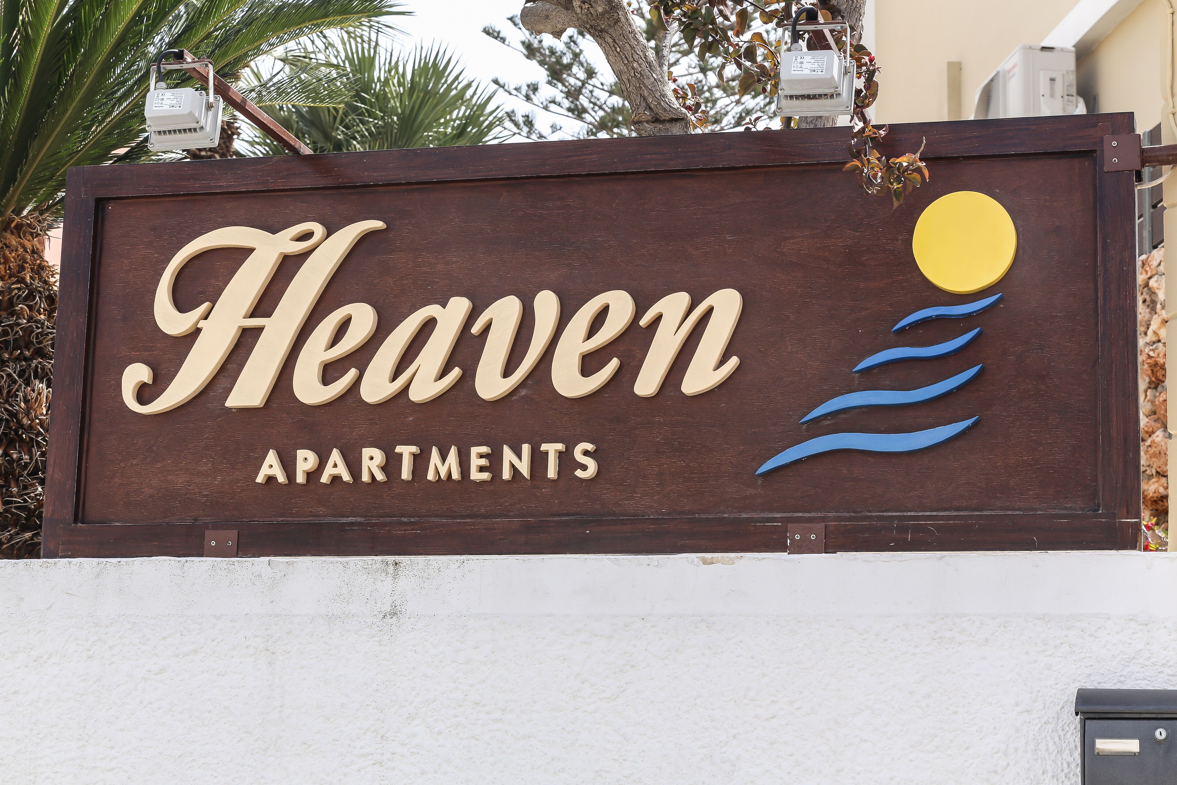 A sign for "Heaven Apartments" with a sun and waves graphic.