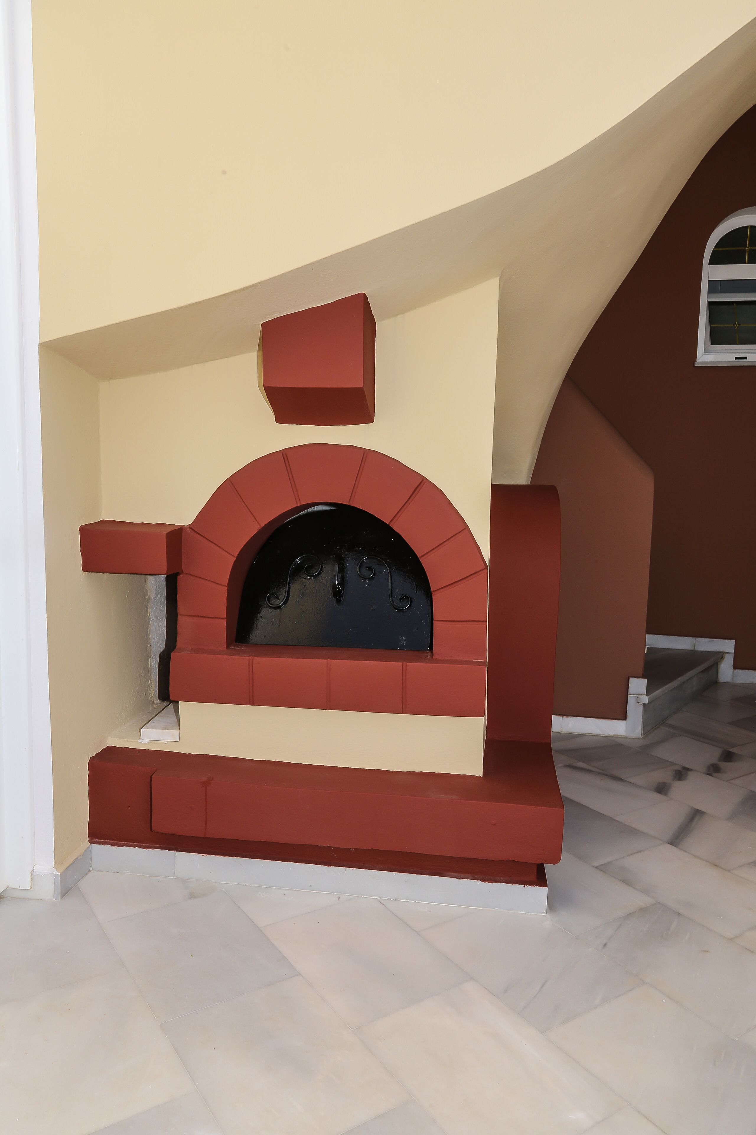 Lareira de tijolos vermelhos com porta de vidro preto, embutida numa parede bege com base branca.
