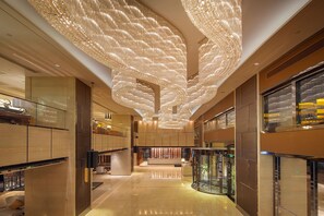 Un hall d’entrée spacieux agrémenté d’un lustre moderne, d’un ascenseur en verre et d’un comptoir de réception.