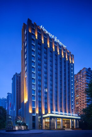 Un hotel de gran altura con un letrero llamativo de "Howard Johnson", varios pisos y una entrada bien iluminada.