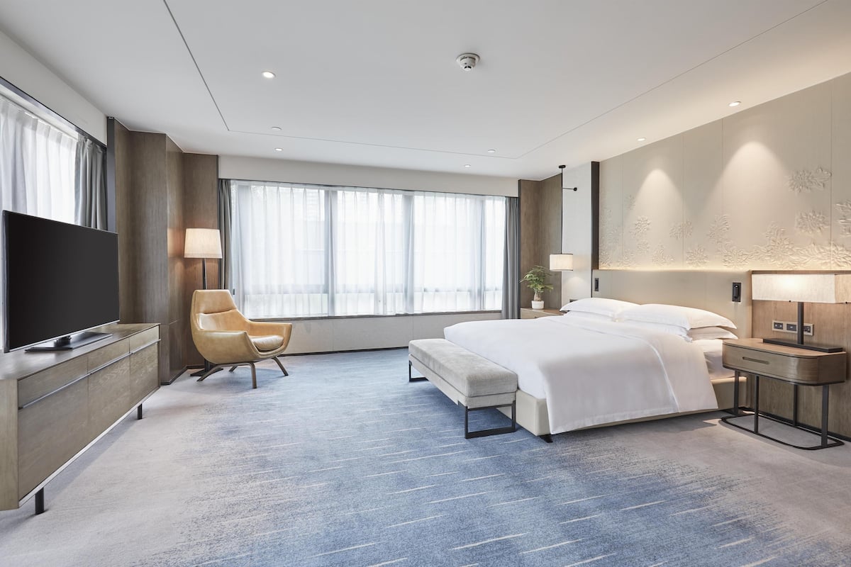 A modern hotel room with a large bed, a flat-screen TV, a desk, and a chair.