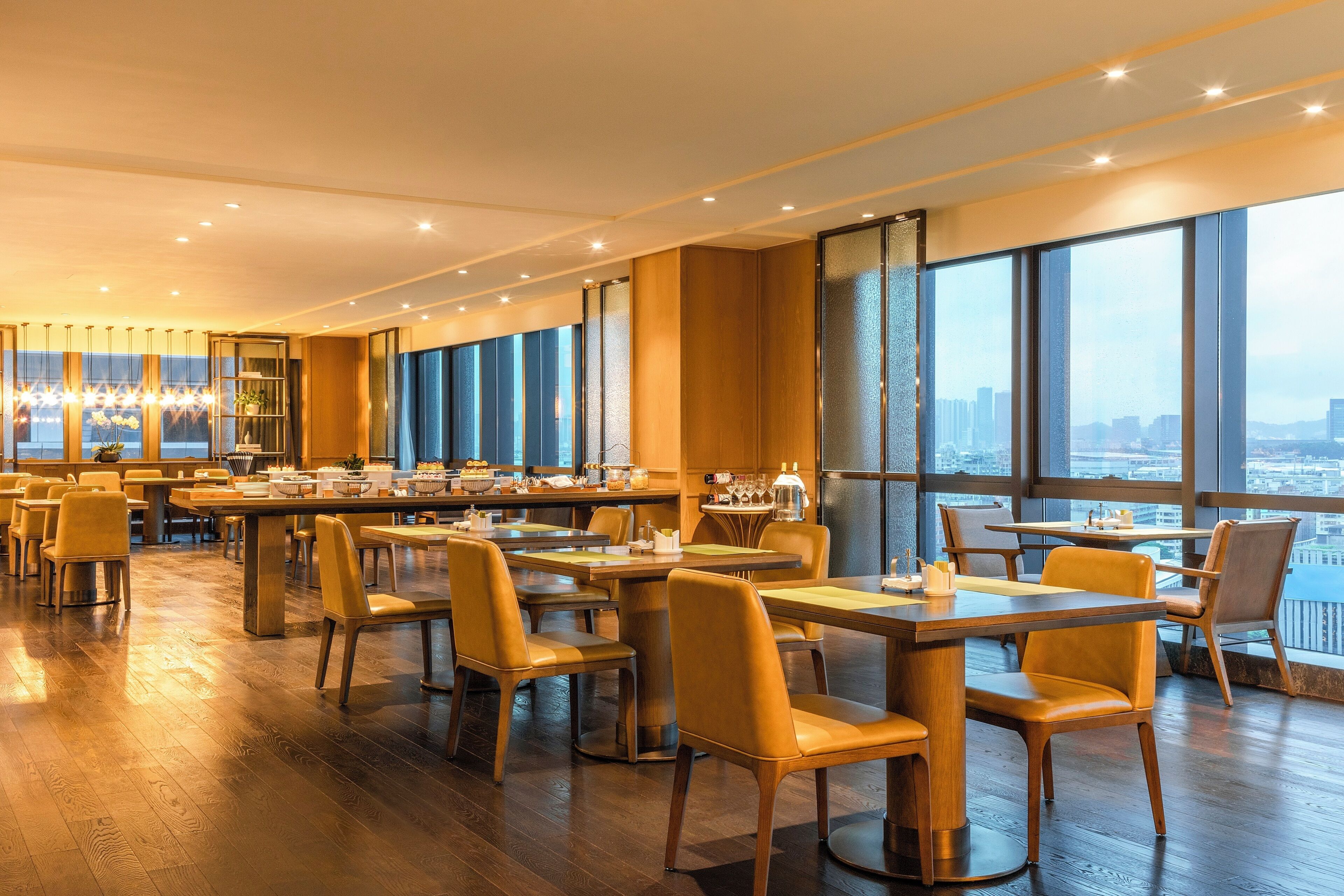 A spacious dining area with multiple tables and chairs, large windows with a city view, and a modern interior design.