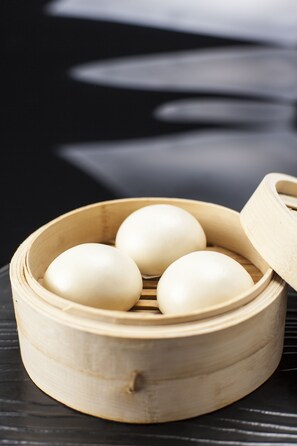 A bamboo steamer with four white eggs inside, placed on a dark surface. - DoubleTree by Hilton Hotel Shenzhen Longhua (Shenzhen)