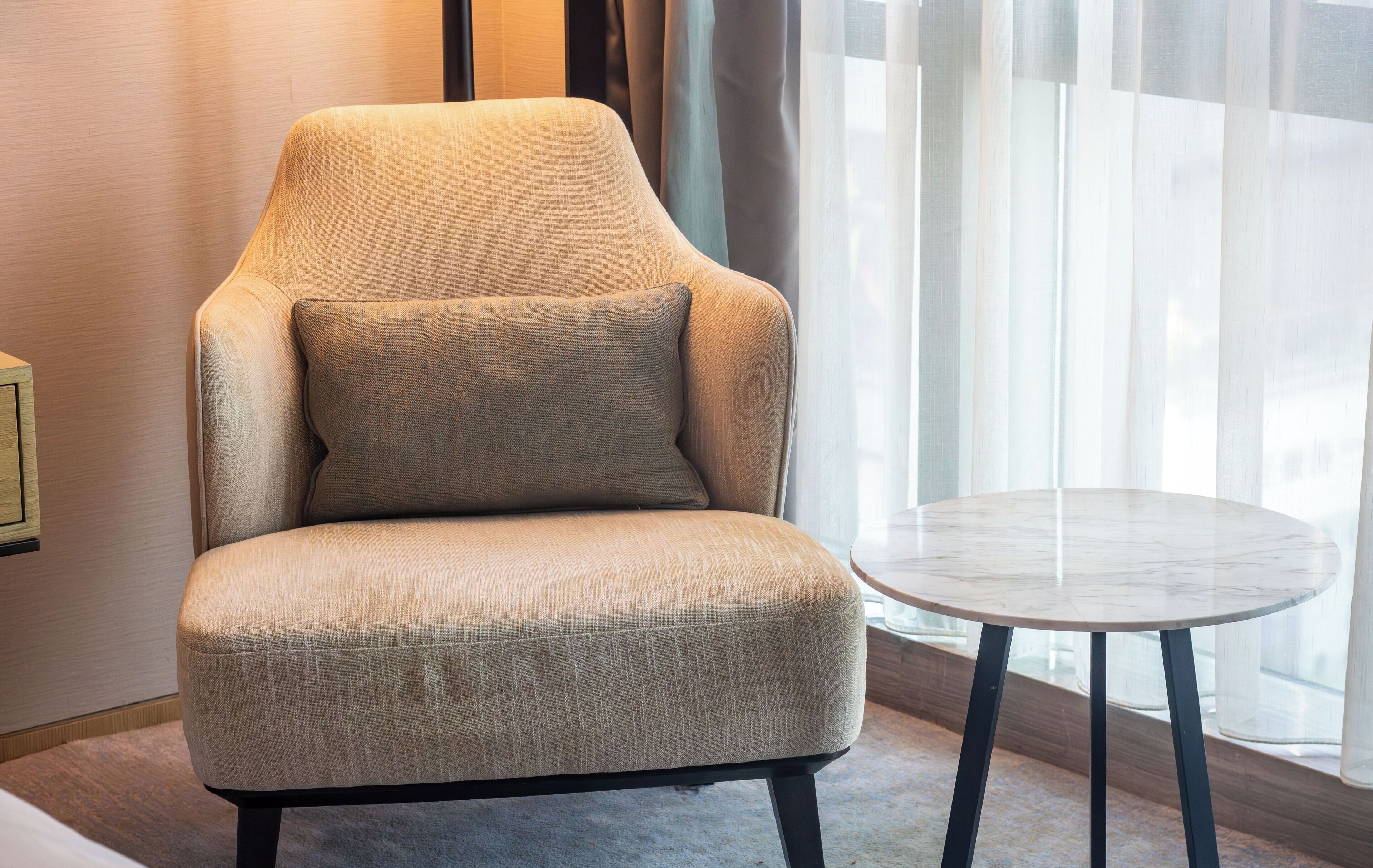A modern armchair with a matching pillow, positioned next to a small round table in a well-lit room with a large window.