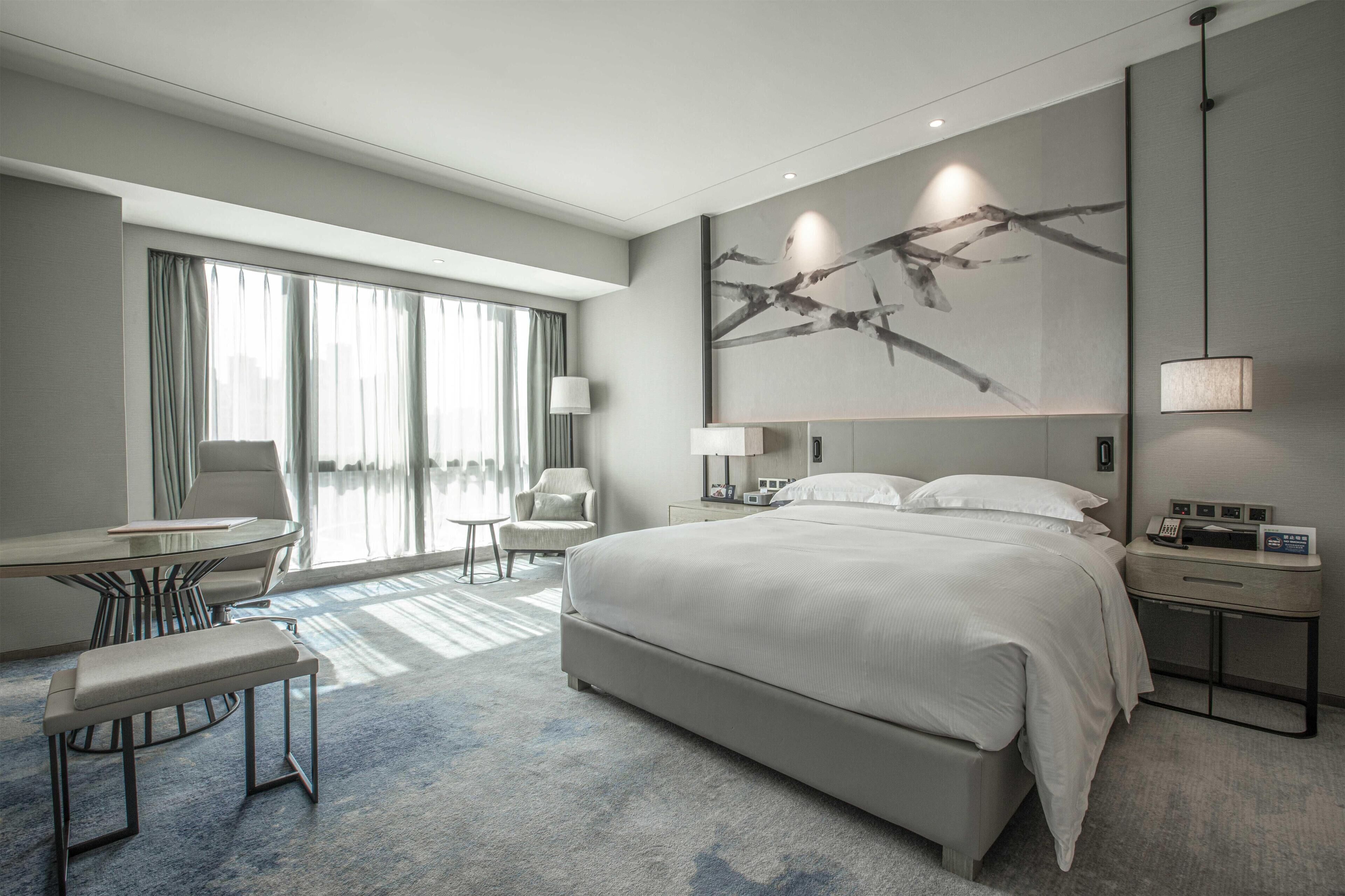 A modern hotel room with a large bed, a desk, and a chair.