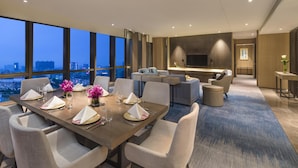 Un comedor moderno de hotel con una mesa grande lista para una comida, un sofá y un televisor al fondo.
