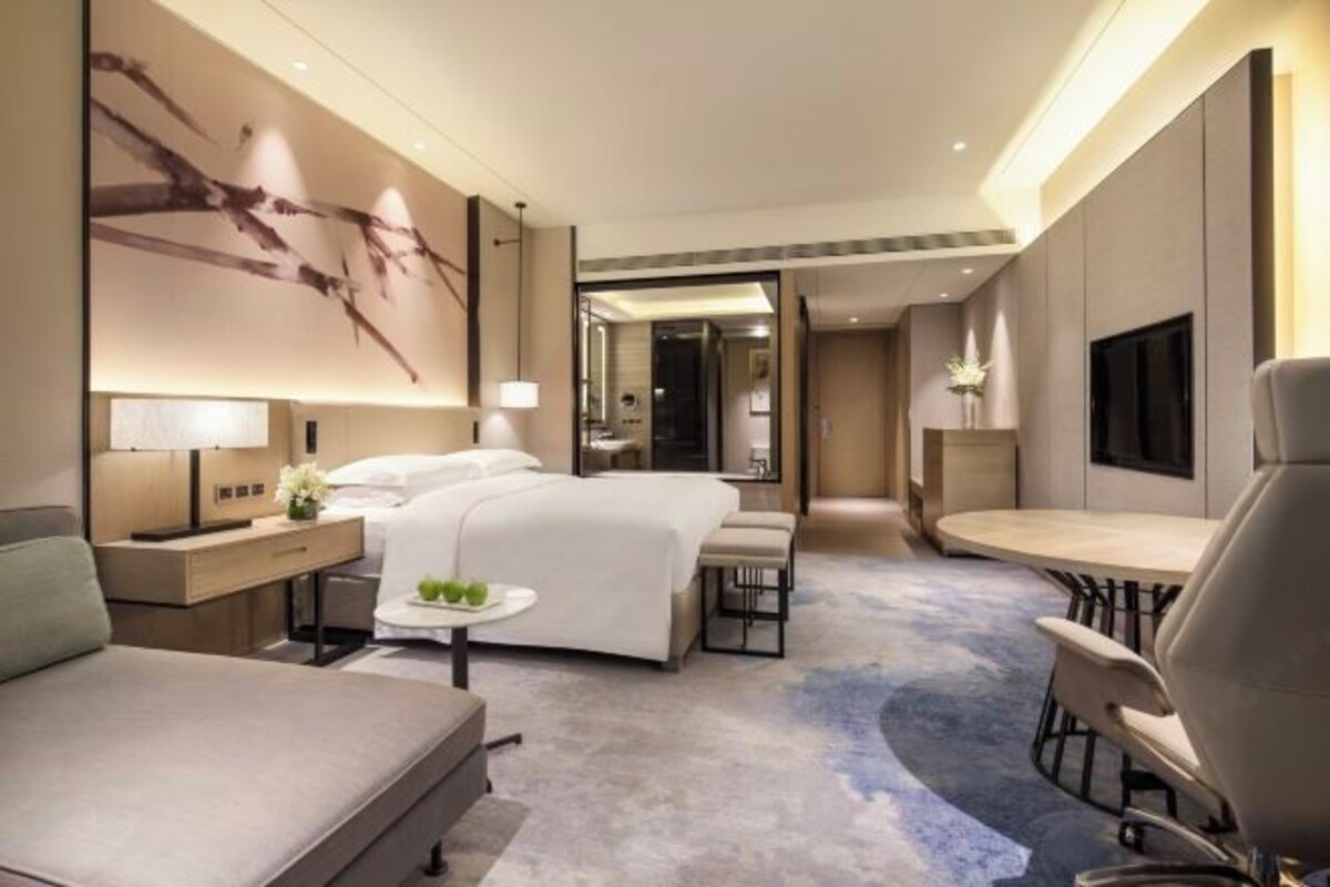 A modern hotel room with a large bed, a desk, a chair, and a round table.