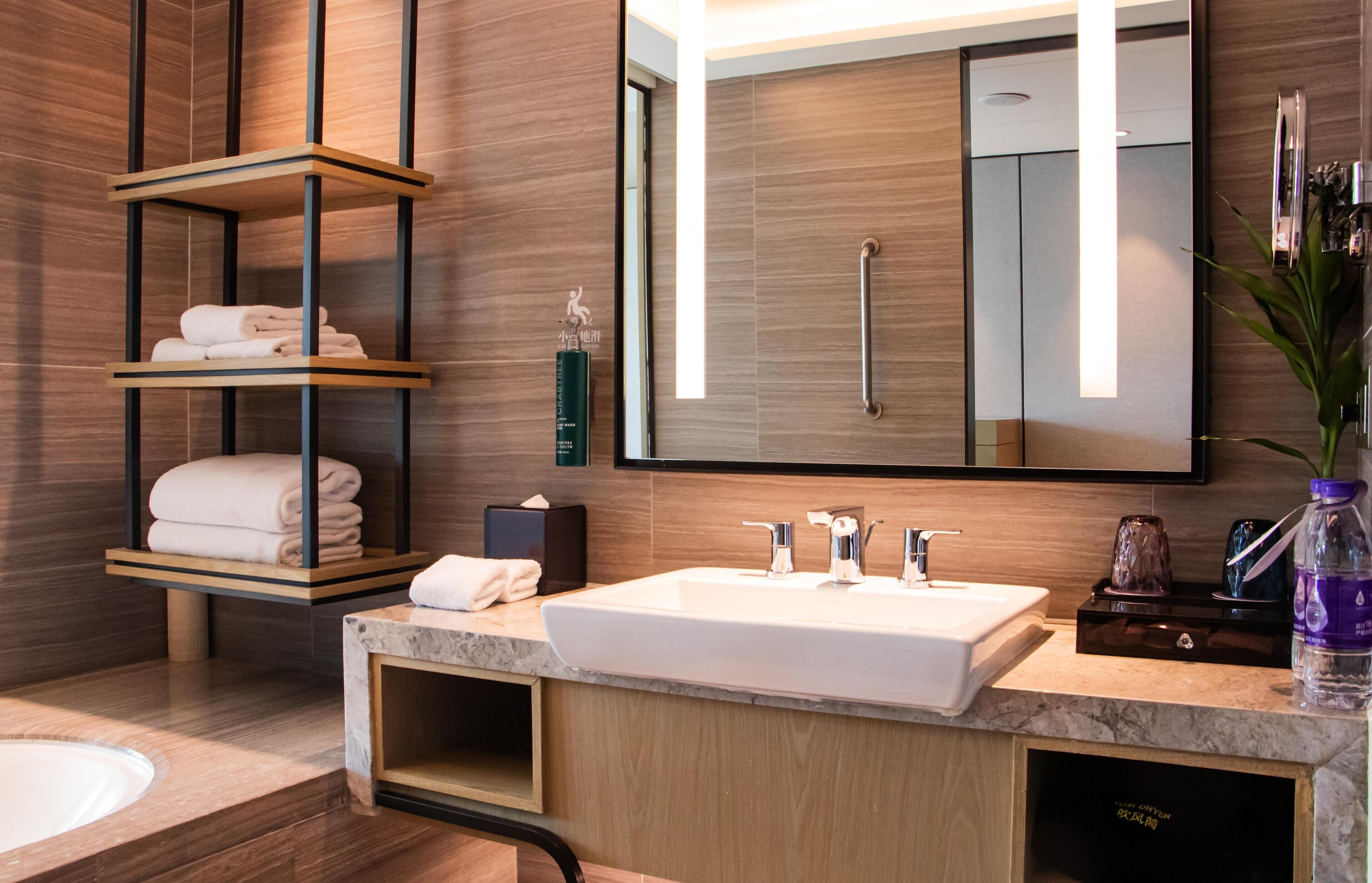 A modern bathroom with a large mirror, a white sink, and a towel rack with folded towels.