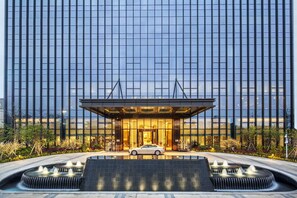 A modern hotel entrance with a car parked in front, a water feature, and a reflection of the building's facade. - DoubleTree by Hilton Hotel Shenzhen Longhua (Shenzhen)