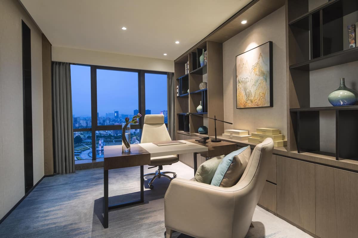 A modern office with a desk, chair, and shelves. It features a large window with a city view.