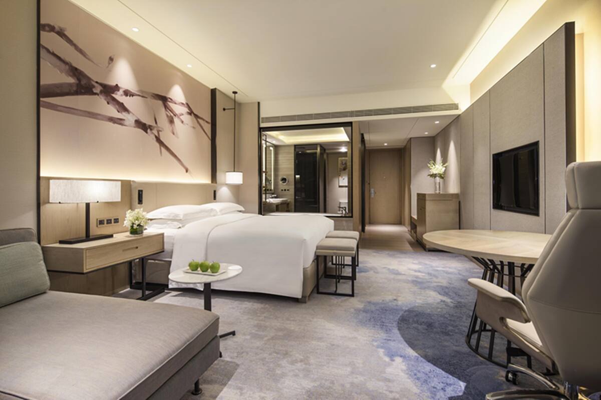 A modern hotel room with a large bed, a desk, a dining area, and a TV.