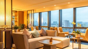 Una sala de estar moderna con sofá, sillones y una mesita de centro. Amplias ventanas ofrecen vistas a la ciudad.