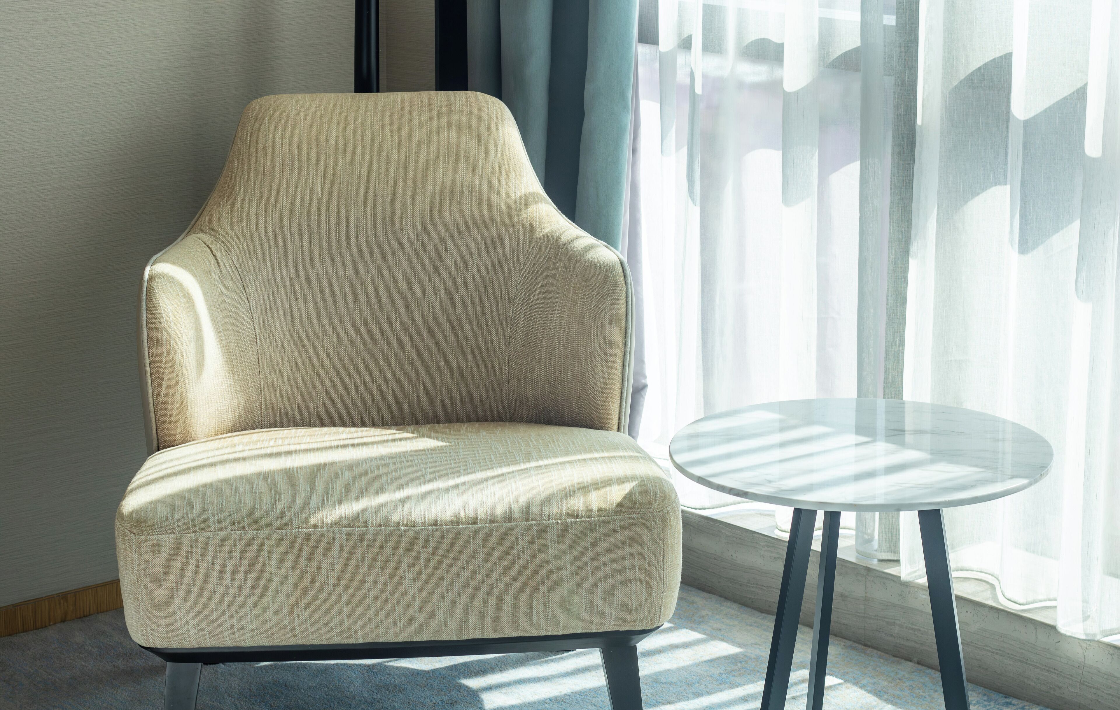 A beige armchair with a high back and a round glass table beside it.
