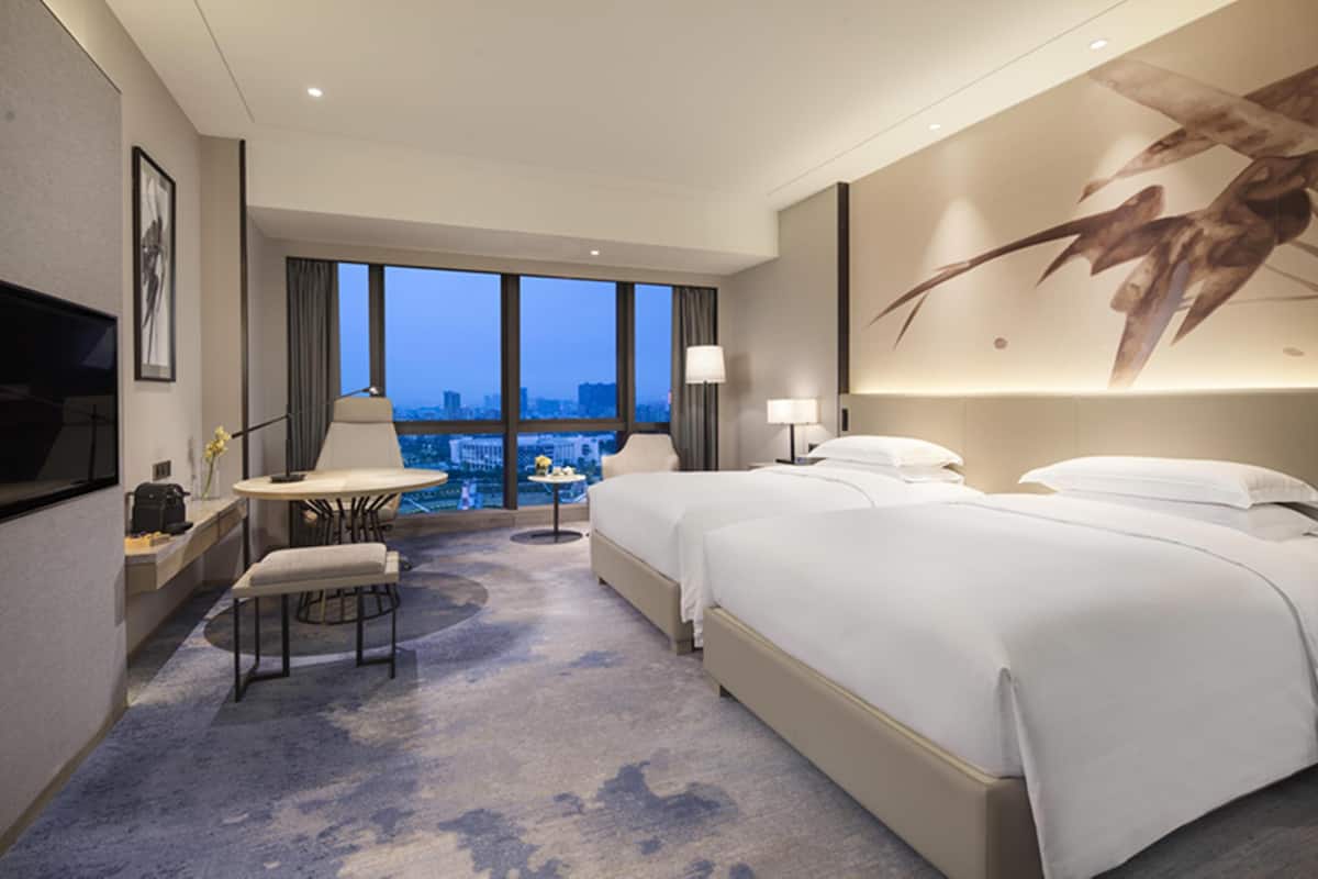 A hotel room with a large bed, a desk with a chair, a small table, and a TV.