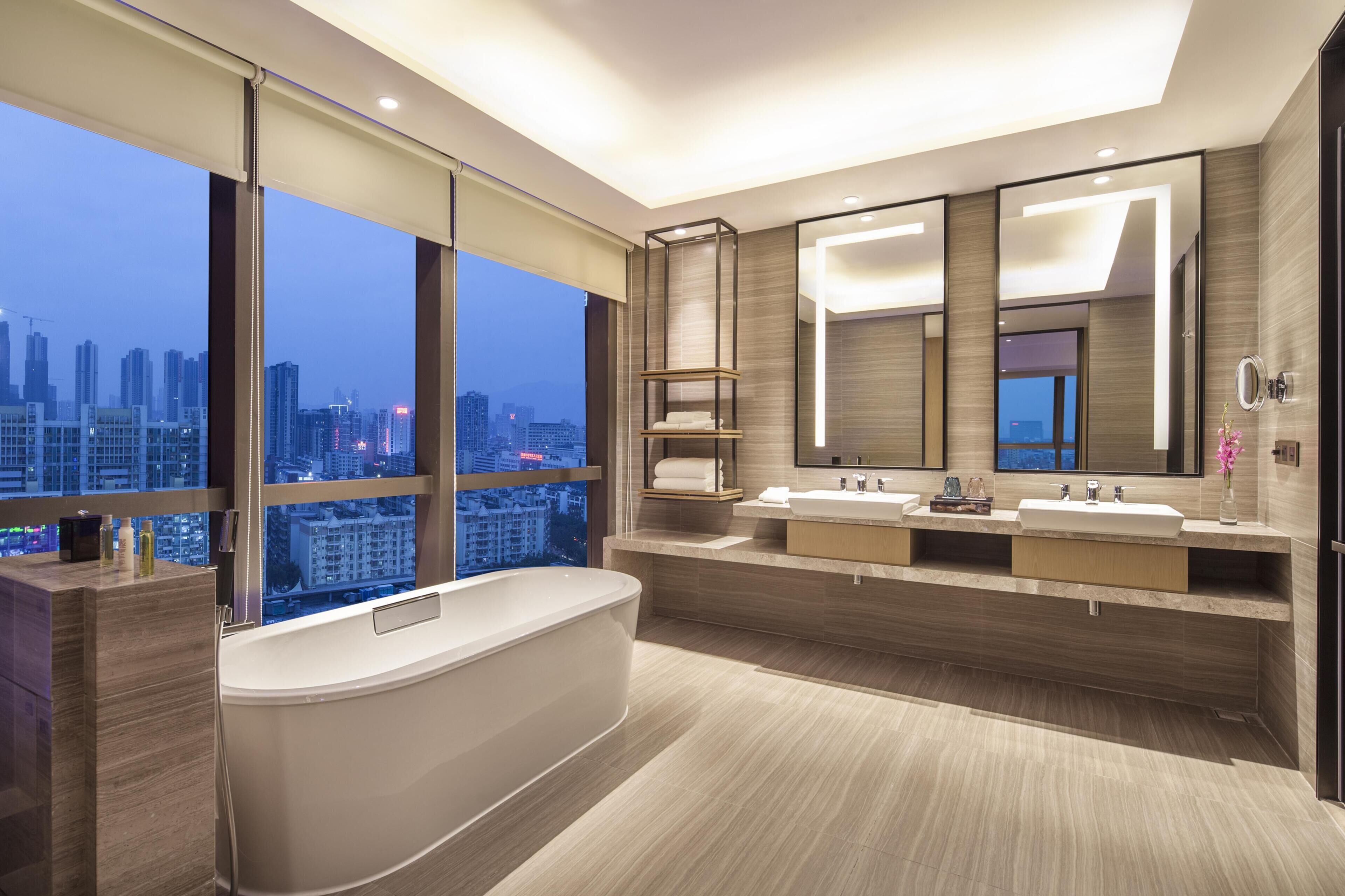 A modern bathroom with a bathtub, two sinks, and a large mirror.