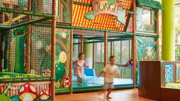 A children's play area with a jungle theme, including a netted climbing structure and a slide.