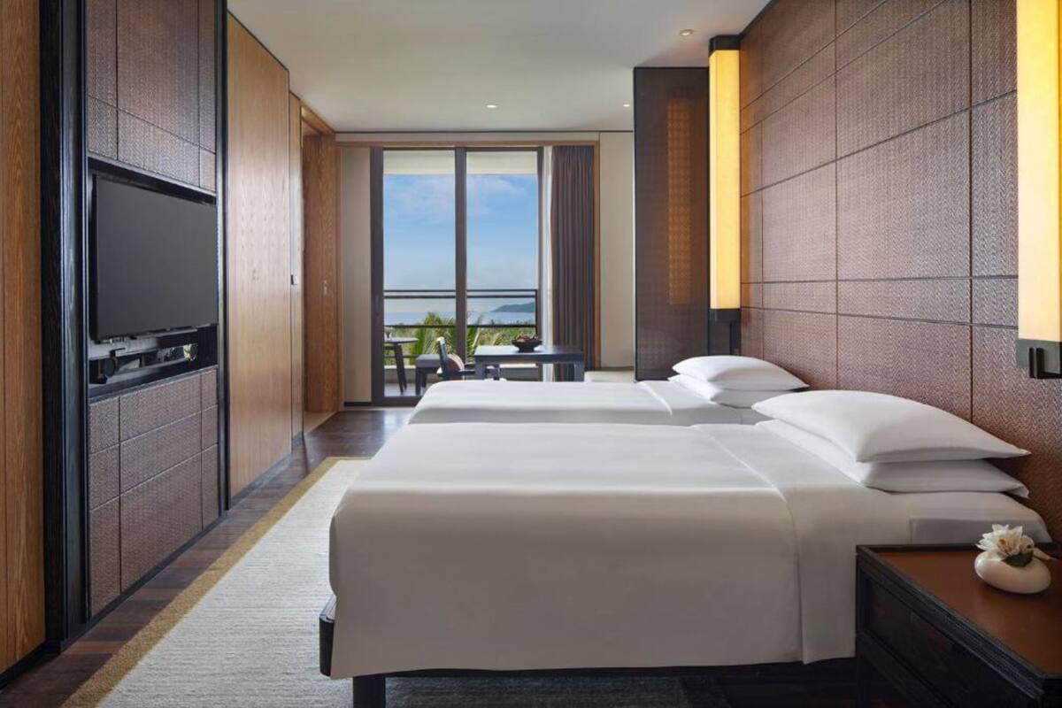 A hotel room with two beds, a TV, a balcony with a table and chairs, and a view of the sea.