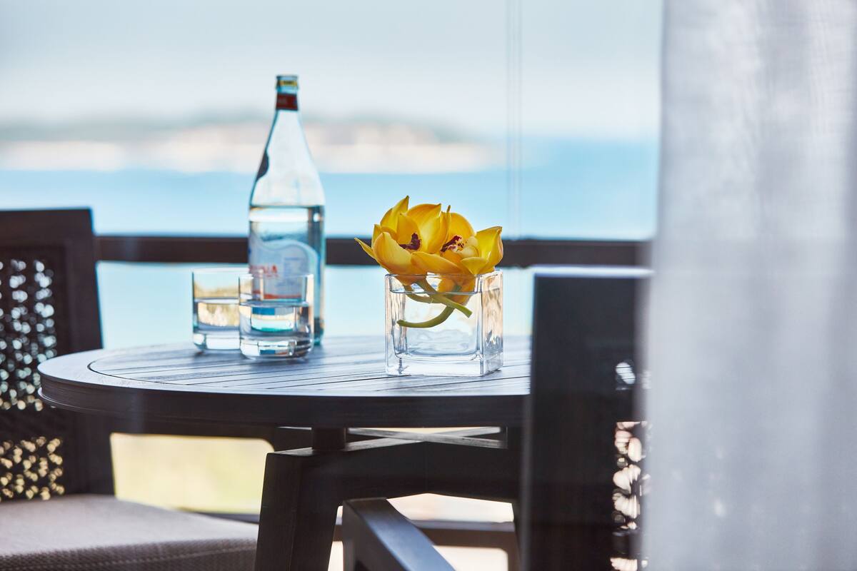 A table with a bottle and a glass of water, and a vase with yellow flowers.