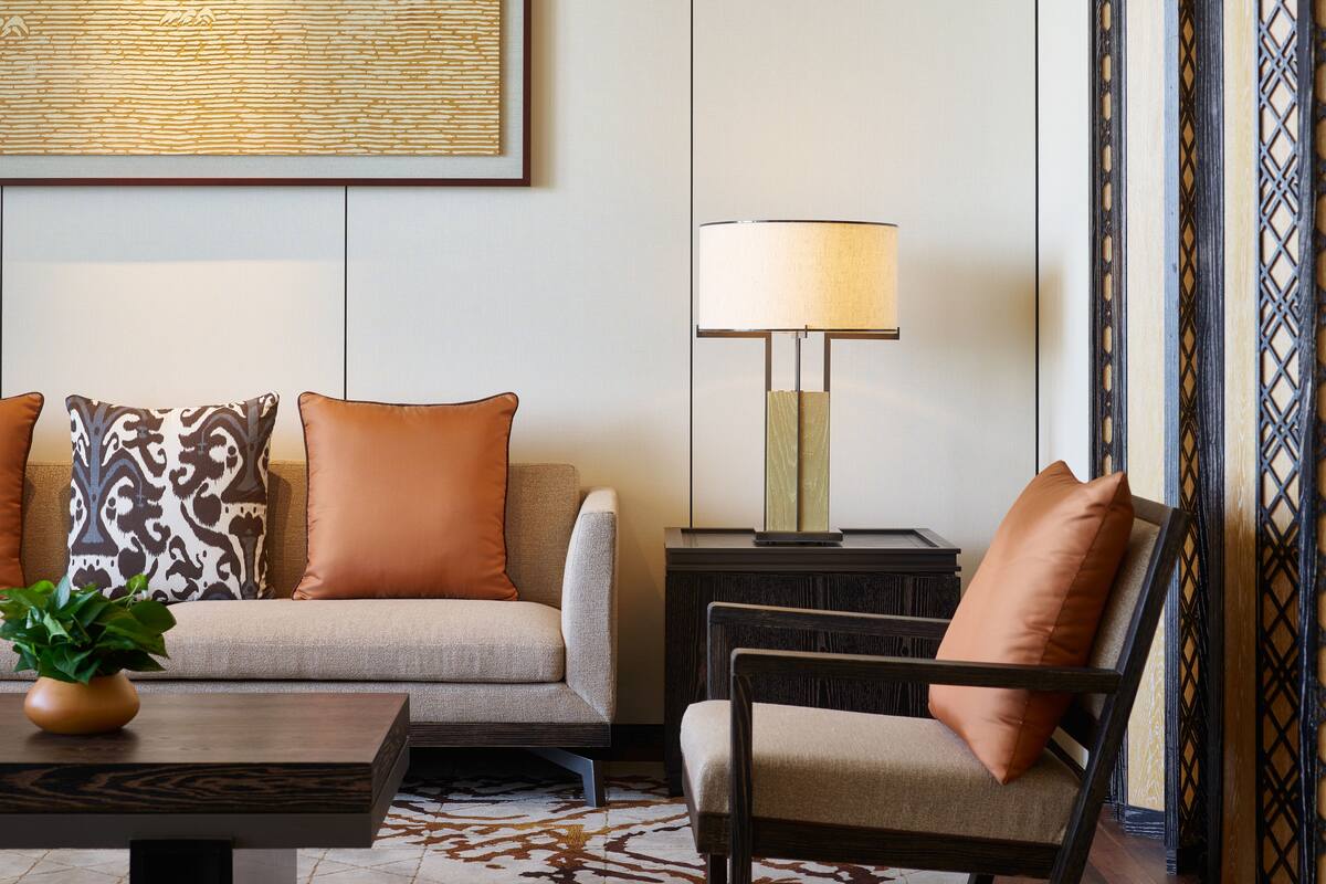 A modern living room with a sofa, armchair, and a side table with a lamp.