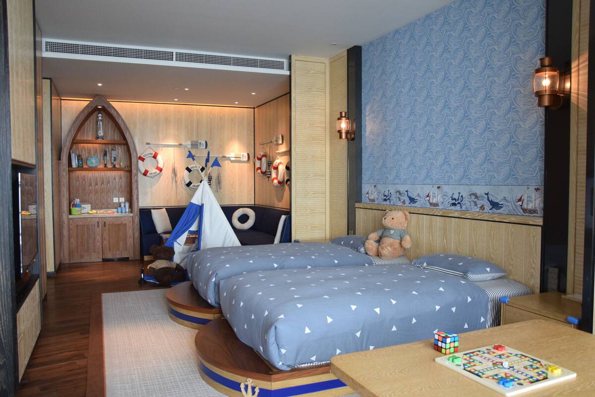 A bedroom with two beds, a wooden wardrobe, a small table with a Rubik's cube, and a wall with nautical-themed decorations.
