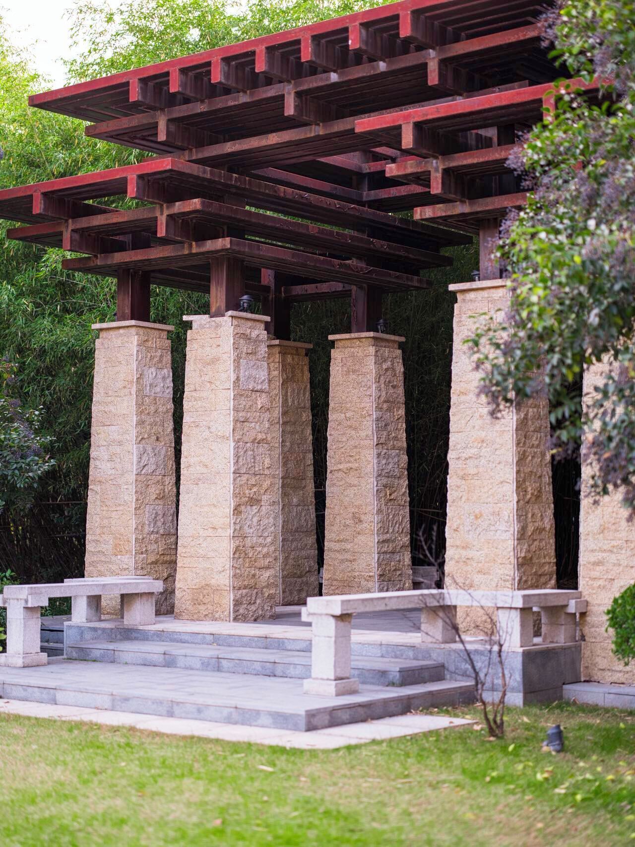 A stone pavilion with a red roof, surrounded by greenery.