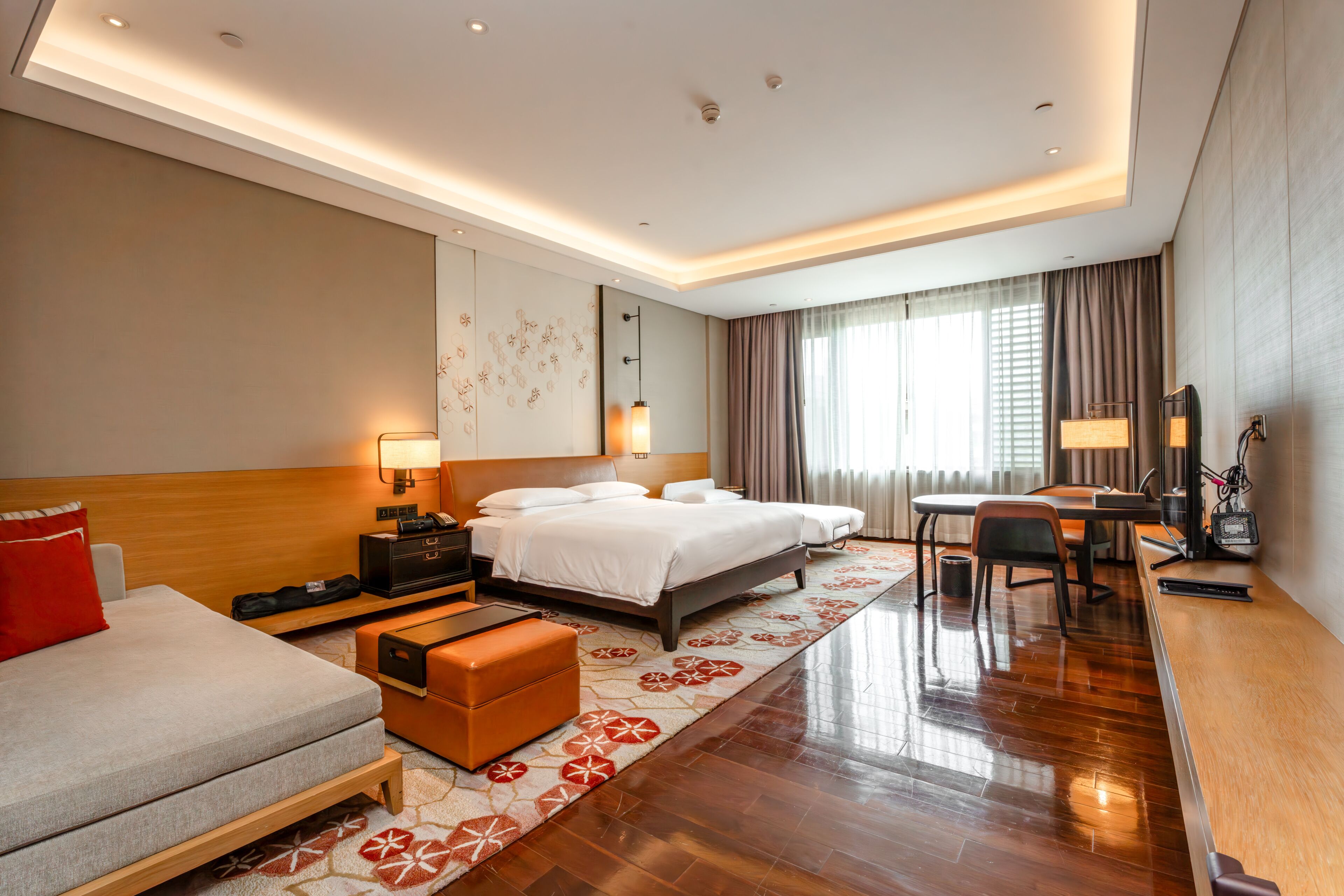 A hotel room with a bed, bedside tables, a desk, a chair, a sofa, and a patterned rug.
