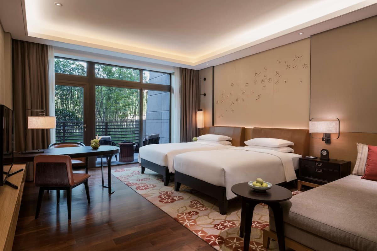 Ein Hotelzimmer mit zwei Betten, einem Schreibtisch, einem Sessel und einem kleinen Tisch.