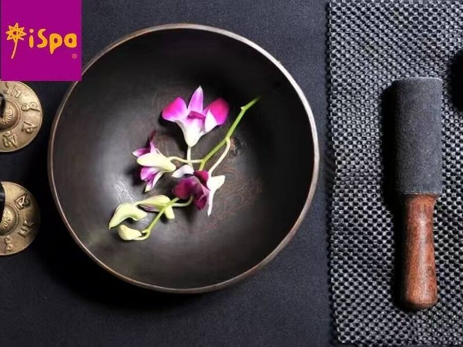 A dark bowl with flowers and two metallic objects on a black surface.