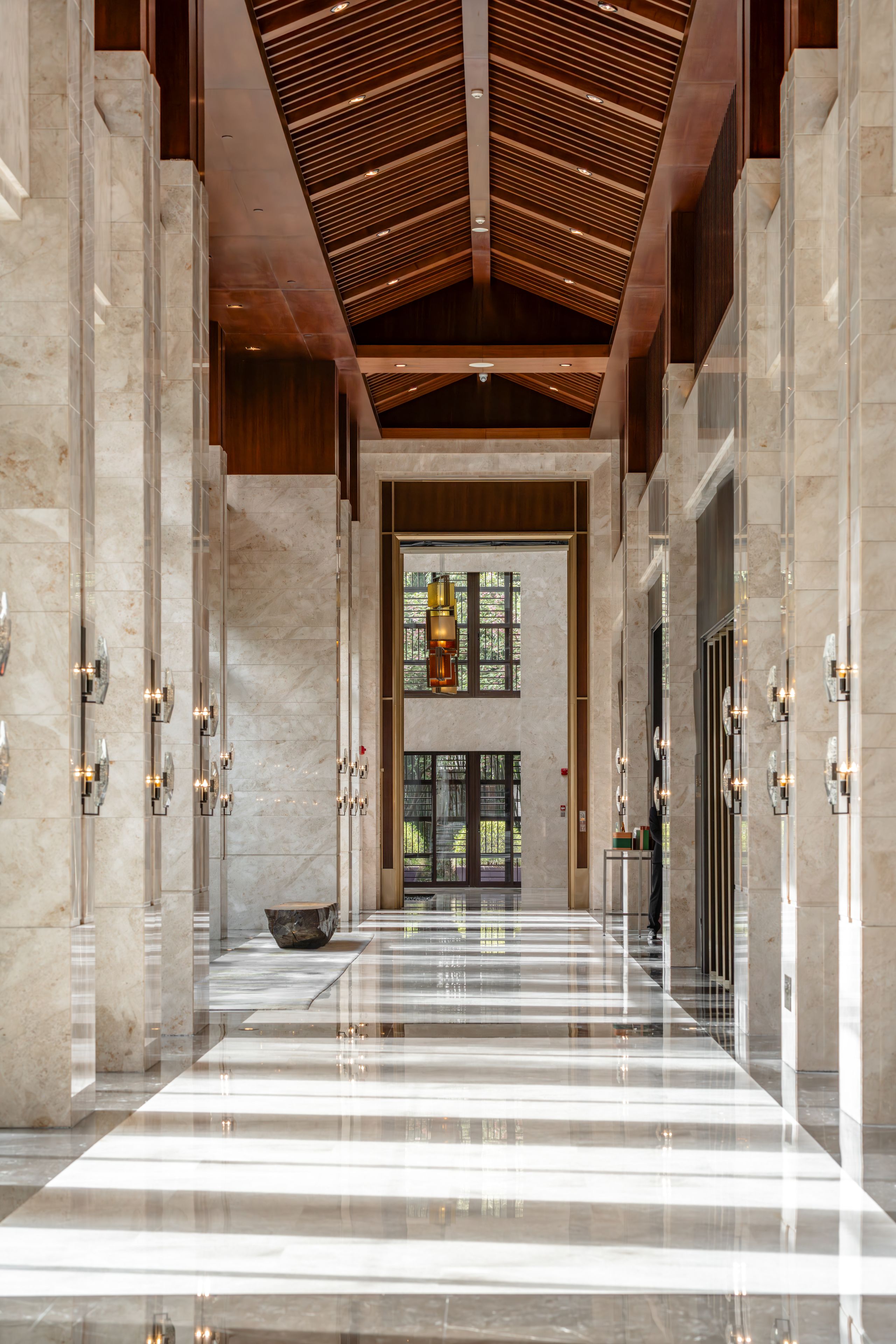 A spacious lobby with a high ceiling, marble flooring, and a central open area with a view of greenery outside.