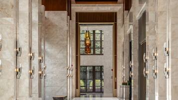 A spacious lobby with a high ceiling, marble flooring, and a central open area with a view of greenery outside.