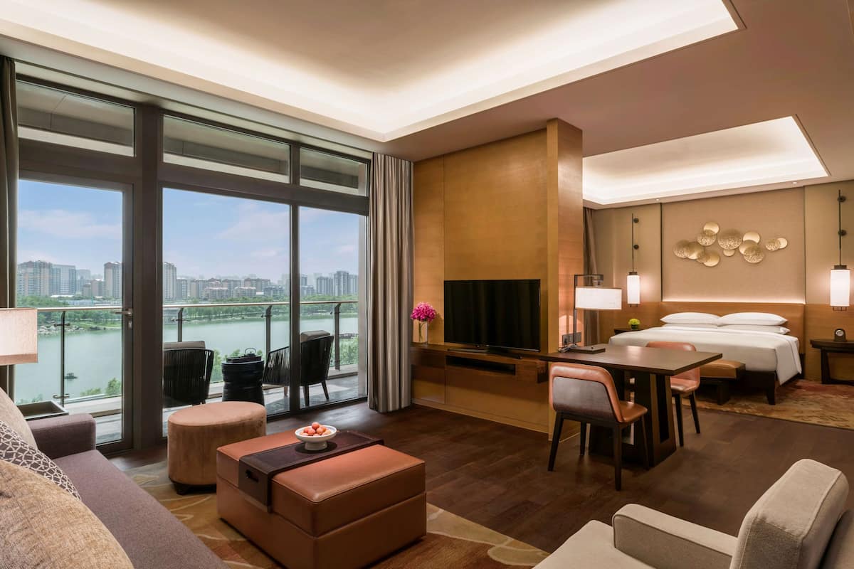 Ein modernes Hotelzimmer mit großem Fenster und Blick auf die Stadt, einem Flachbildfernseher, einem Bett, einer Essecke und einer Sitzecke mit Aussicht.