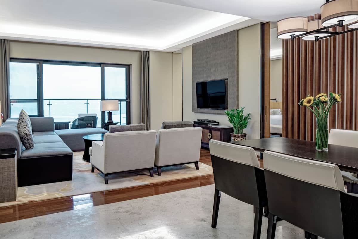 Ein modernes Hotelzimmer mit großem Fenster, Flachbildfernseher, Essbereich mit Tisch und Stühlen sowie einer Sofagarnitur.