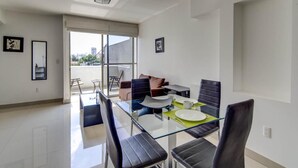 A modern dining area with a glass table and black chairs, a sofa, and a city view through large windows. - Grupo Kings Suites Alfredo de Musset (Mexico City)