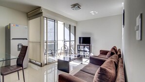 A modern living room with a glass dining table, a sofa set, a flat-screen TV, and a refrigerator. - Grupo Kings Suites Alfredo de Musset (Mexico City)