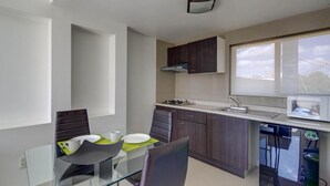 A compact kitchen with a dining area, featuring a glass table, dark wooden cabinets, and a window providing natural light. - Grupo Kings Suites Alfredo de Musset (Mexico City)