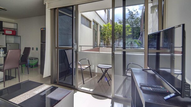 A modern room with a sliding glass door leading to a balcony, a desk with a computer, and a small table with chairs. - Grupo Kings Suites Alfredo de Musset (Mexico City)