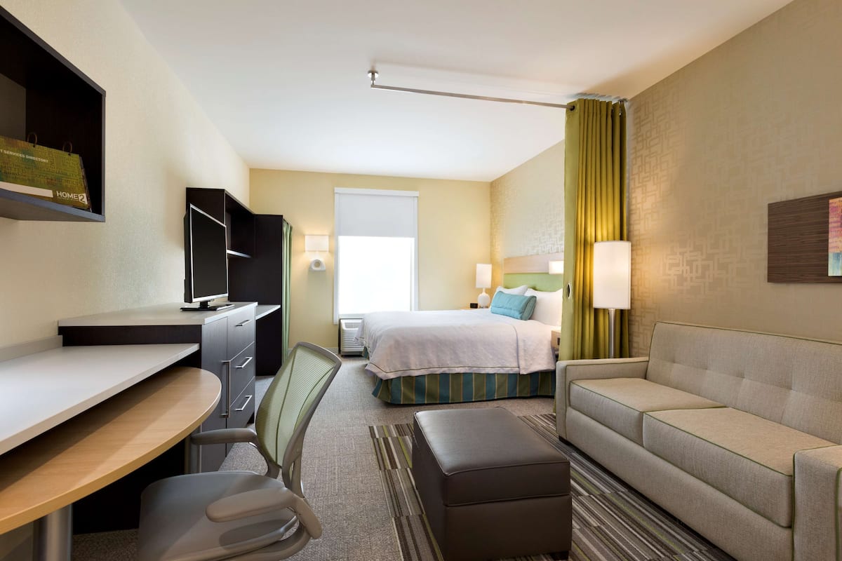 Habitación de hotel con escritorio, silla, cama, sofá y televisor.